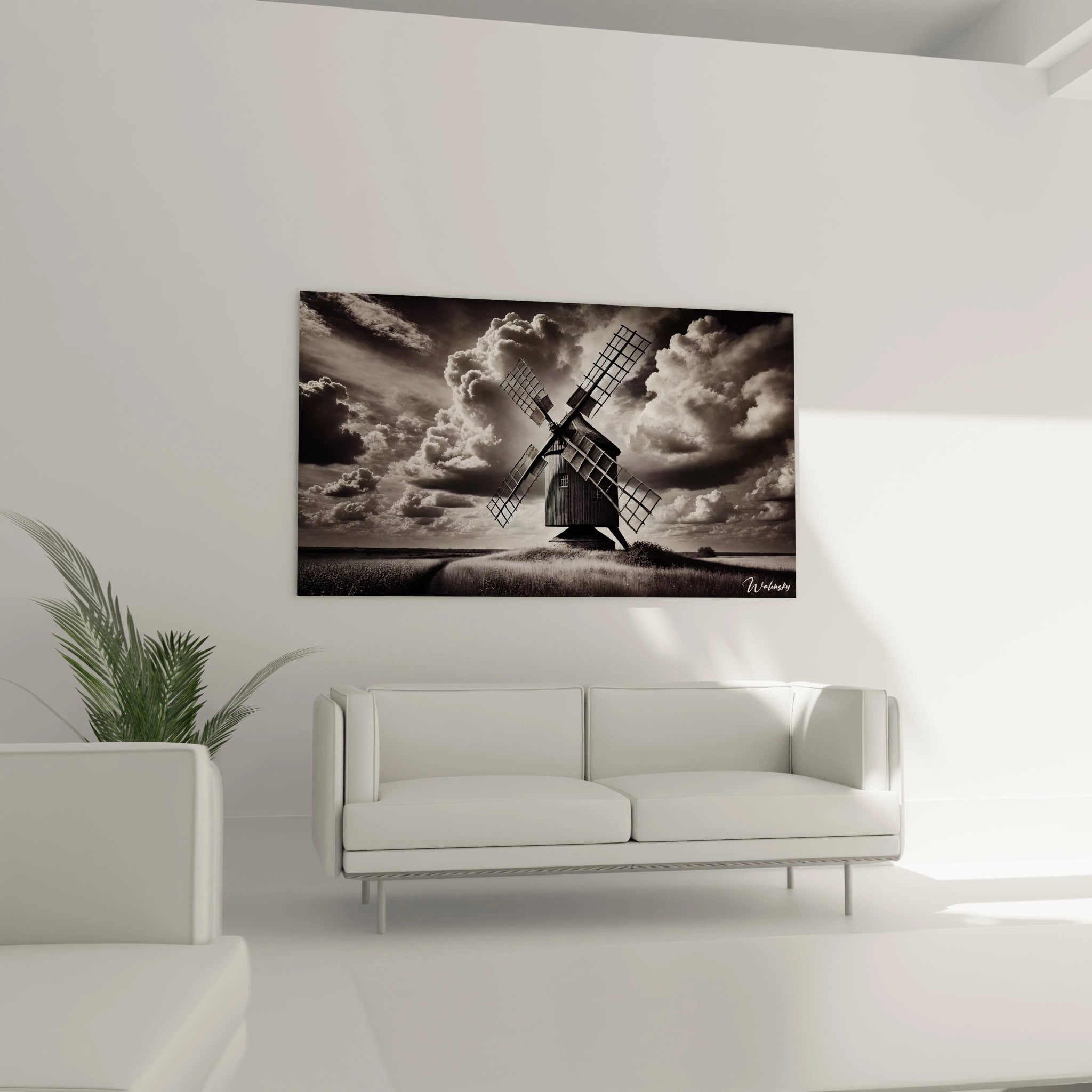 Tableau noir et blanc place au-dessus d’un canape dans un salon moderne montrant un moulin rural sous un ciel dramatique, parfait pour un decor raffine.