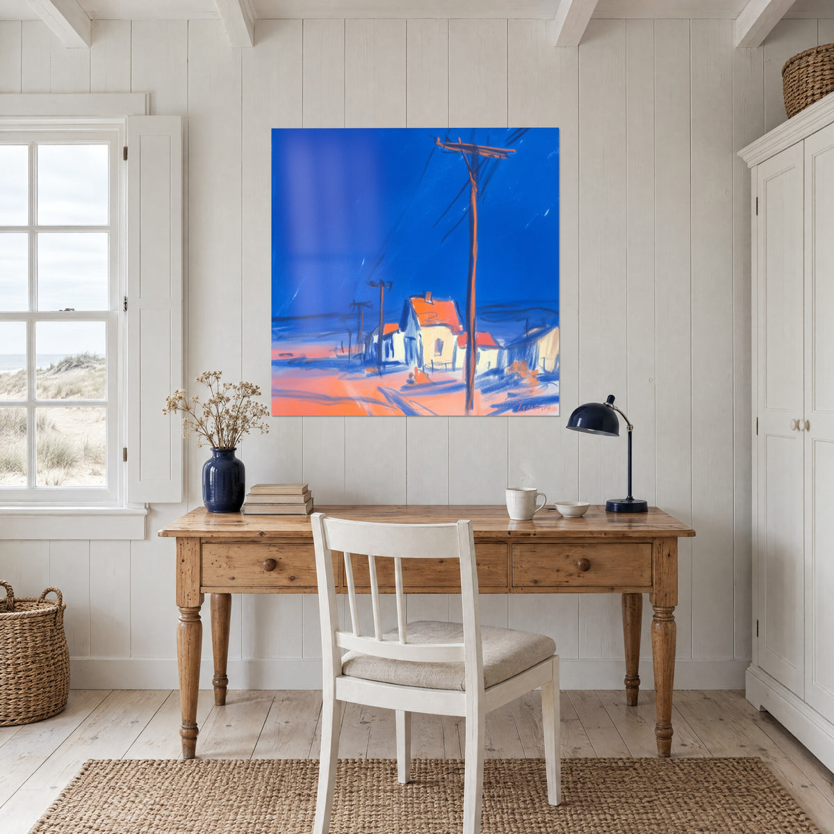 Πίνακας με απομονωμένες καλύβες κάτω από βαθύ γαλάζιο ουρανό, ροζ-πορτοκαλί έδαφος και κόκκινες στέγες, κρεμασμένος πάνω από ξύλινο γραφείο