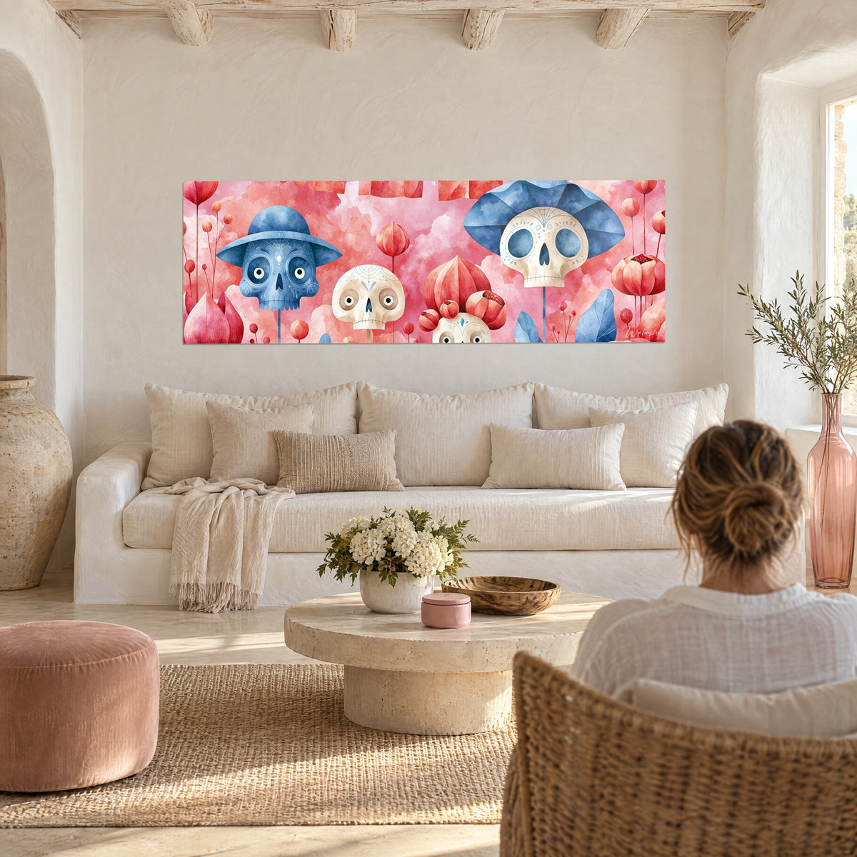 Schilderij van suikerschedels met blauwe hoeden tussen koraalroze bloemen, boven een bank in een lichte woonkamer
