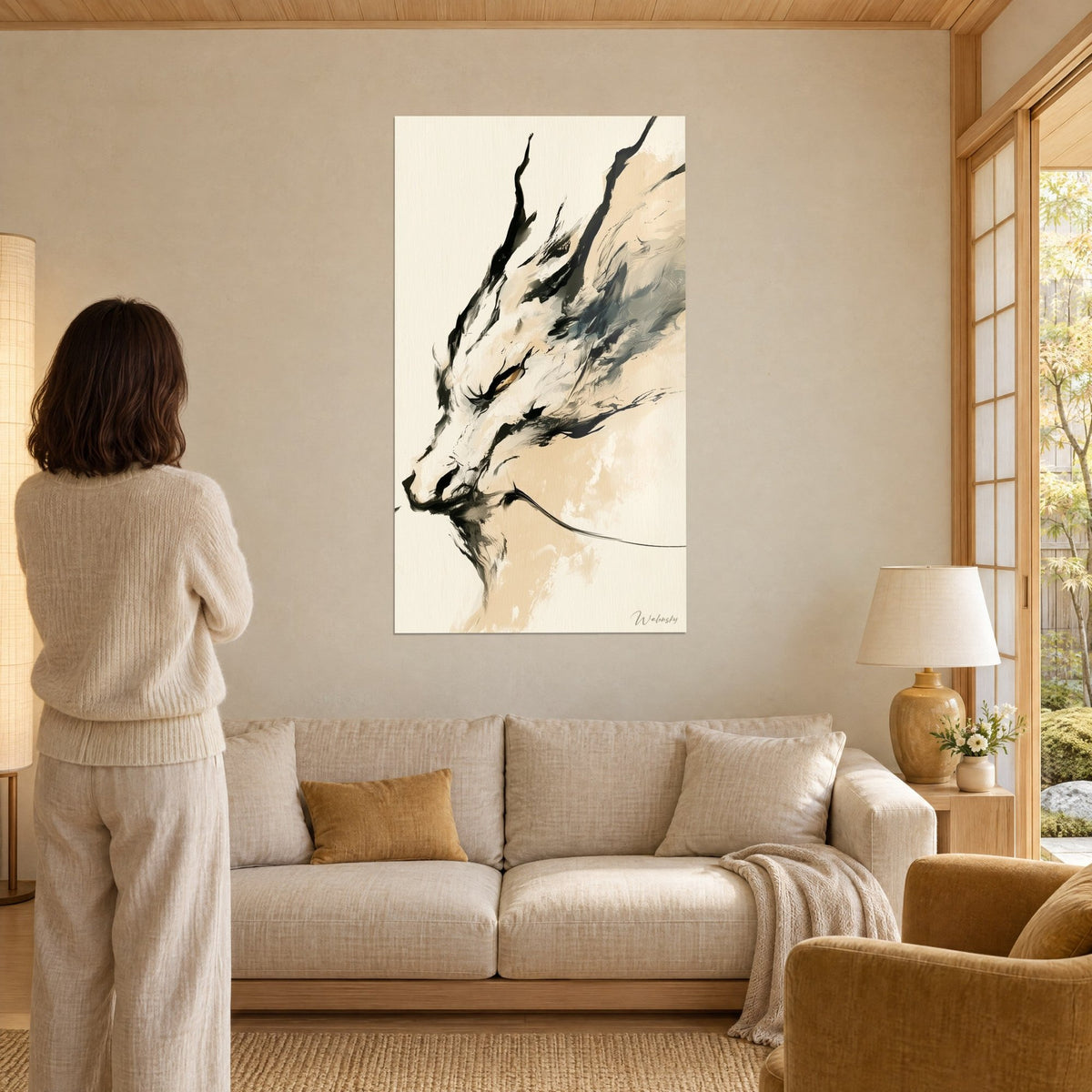 Tableau dragon d'encre ivoire aux cornes noires, une femme de dos le contemple, beige et miel, au-dessus d'un canapé dans un salon lumineux