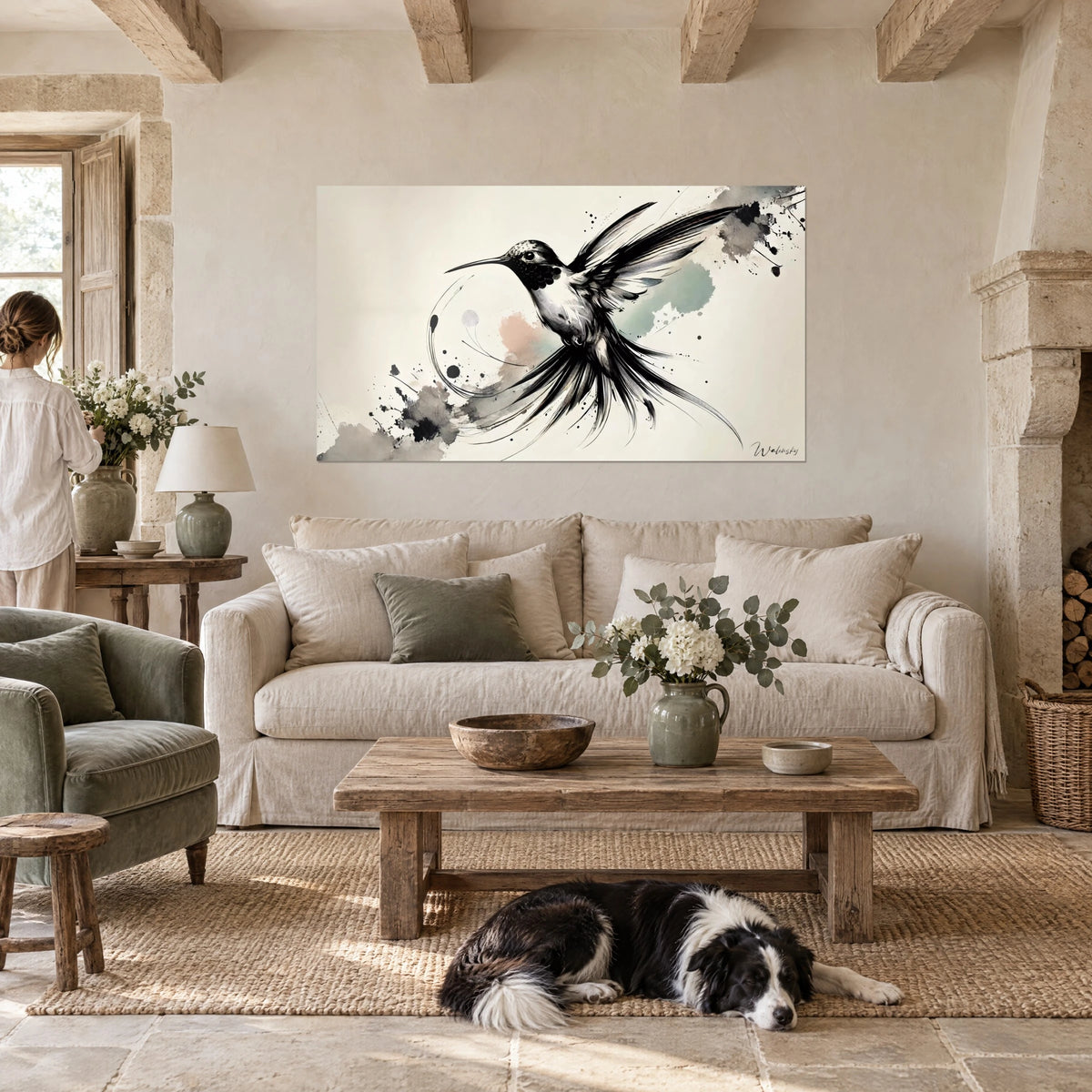 Wall art of a hummingbird in full flight, black wings and ink-drawn feathers on a cream background, above a sofa in a bright living room