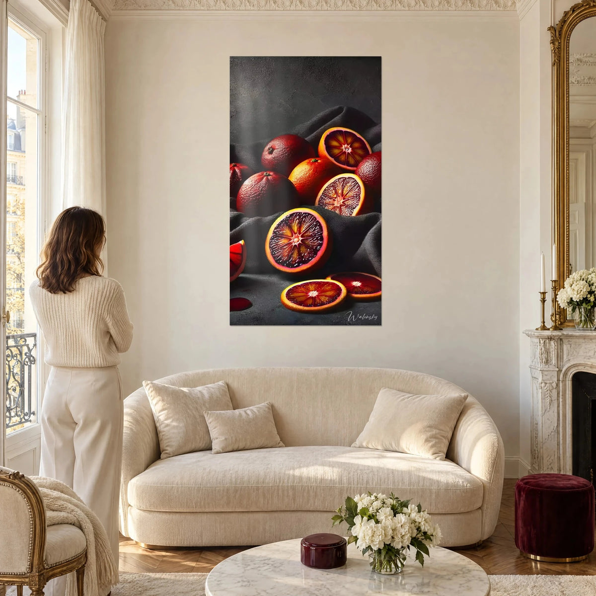 Wall art blood orange, purple and amber citrus on anthracite grey cloth, woman seen from behind above a sofa in a bright living room