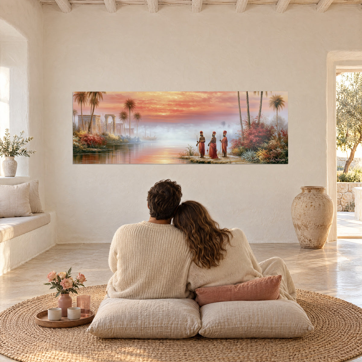 Cuadro atardecer sobre el Nilo, reflejos naranjas en el agua en calma, ruinas faraónicas rosas y doradas, frente a una pareja abrazada de espaldas sobre cojines