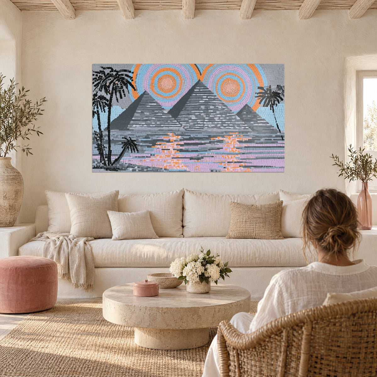 Schilderij grijze piramides in mozaïek onder twee oranje zonnen, zwarte palmbomen, roze reflecties, boven een bank in een lichte woonkamer