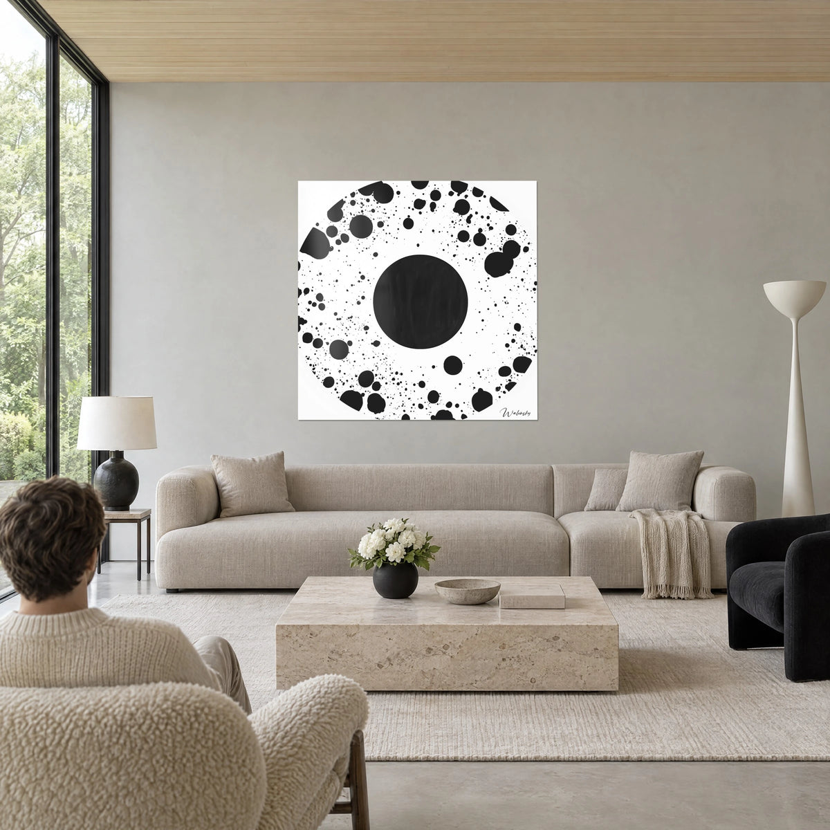 Tableau disque noir anthracite cerné d'éclaboussures d'encre sur fond blanc, deux silhouettes de dos, au-dessus d'un canapé dans un salon lumineux