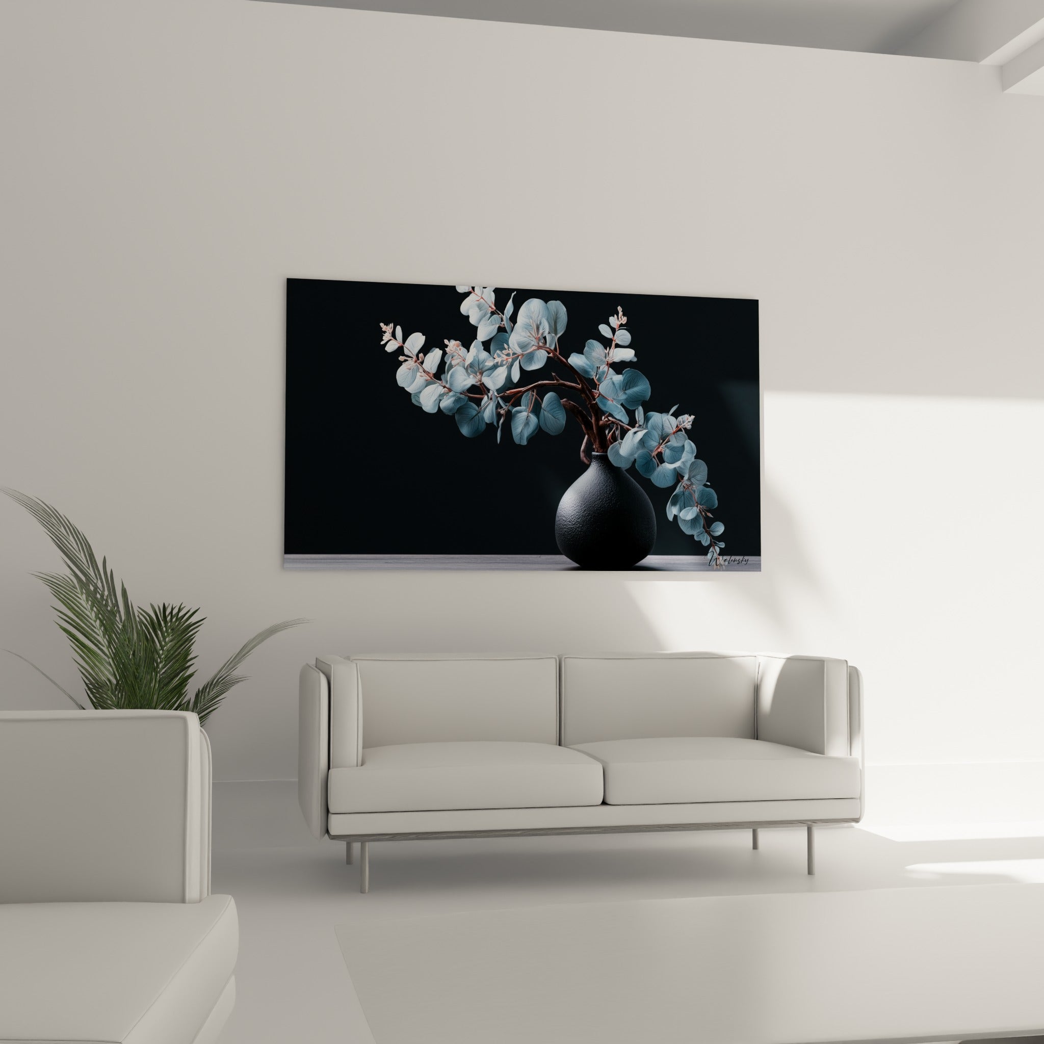 Feuillage d'eucalyptus argenté et vase noir texturé au-dessus d'un canapé dans un salon lumineux