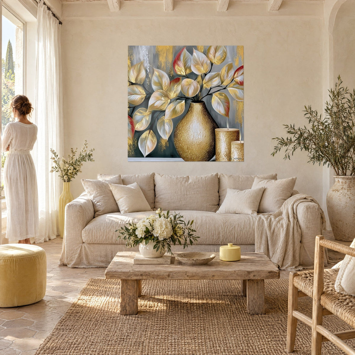 Schilderij getextureerde gouden vaas en witte eucalyptusbladeren, een vrouw in witte jurk van achteren, boven een bank in een lichte woonkamer