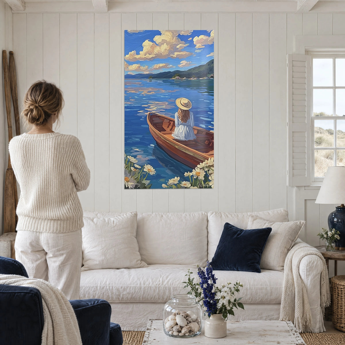 Schilderij jonge vrouw met strohoed zittend in een bruine roeiboot op een blauw meer, crèmekleurige wolken, boven een bank in een lichte woonkamer