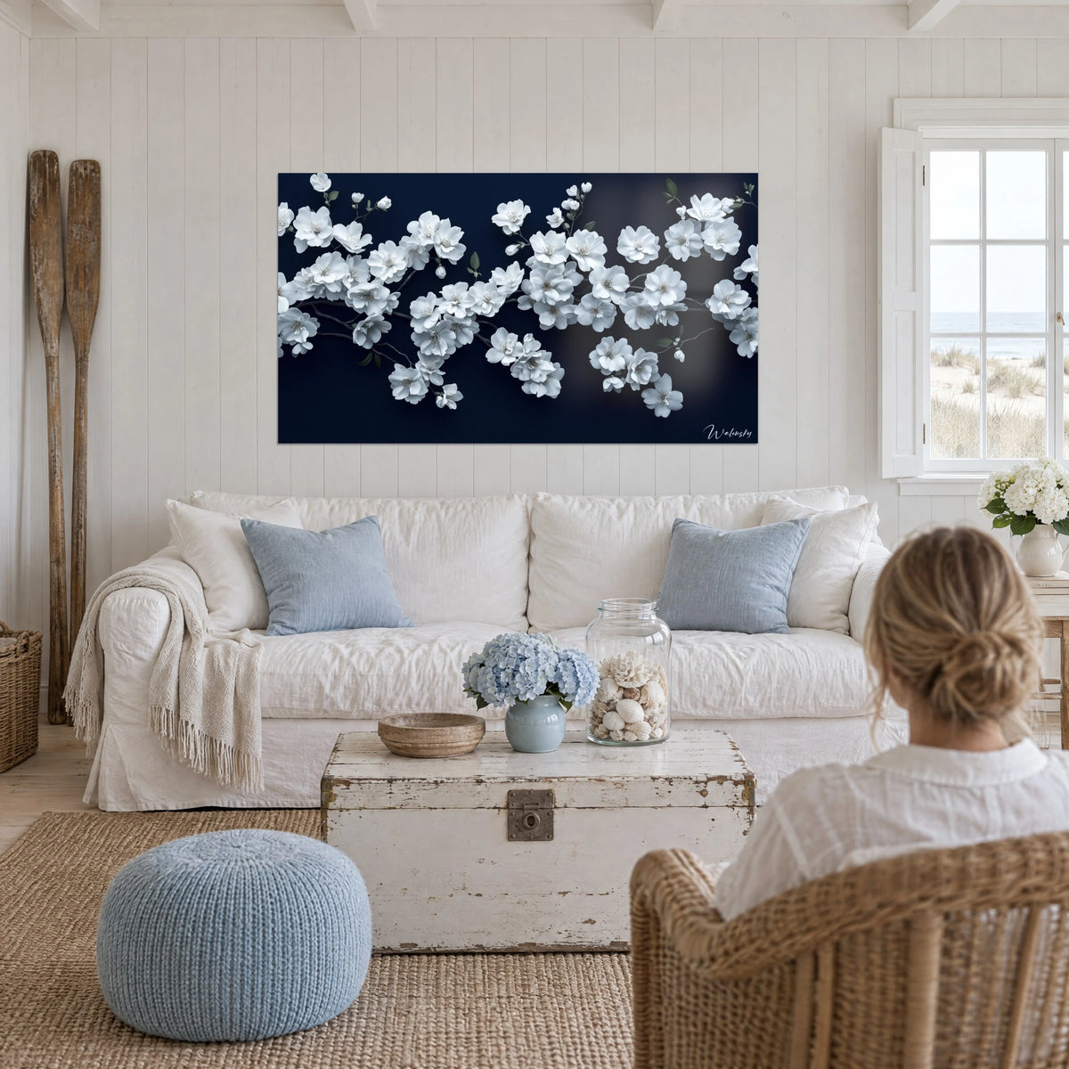 Tableau cerisier en fleurs aux corolles blanc givré sur fond bleu nuit, deux rames en bois, au-dessus d'un canapé dans un salon lumineux