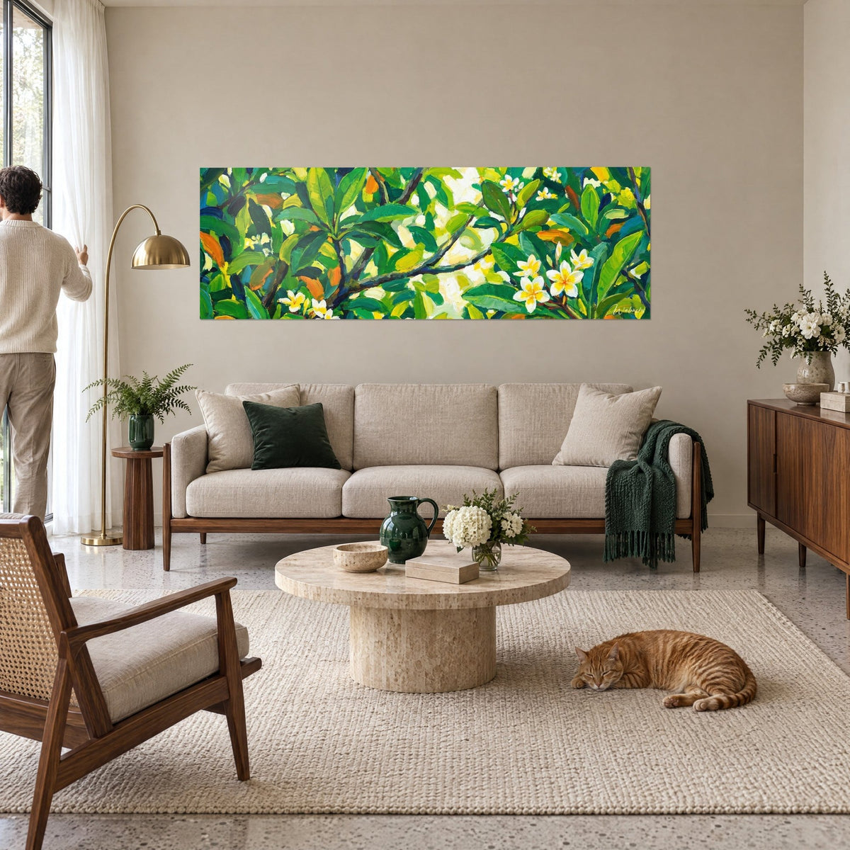 Tableau frangipanier aux fleurs ivoire et cœur jaune parmi des feuilles vertes, une personne de dos, au-dessus d'un canapé dans un salon lumineux