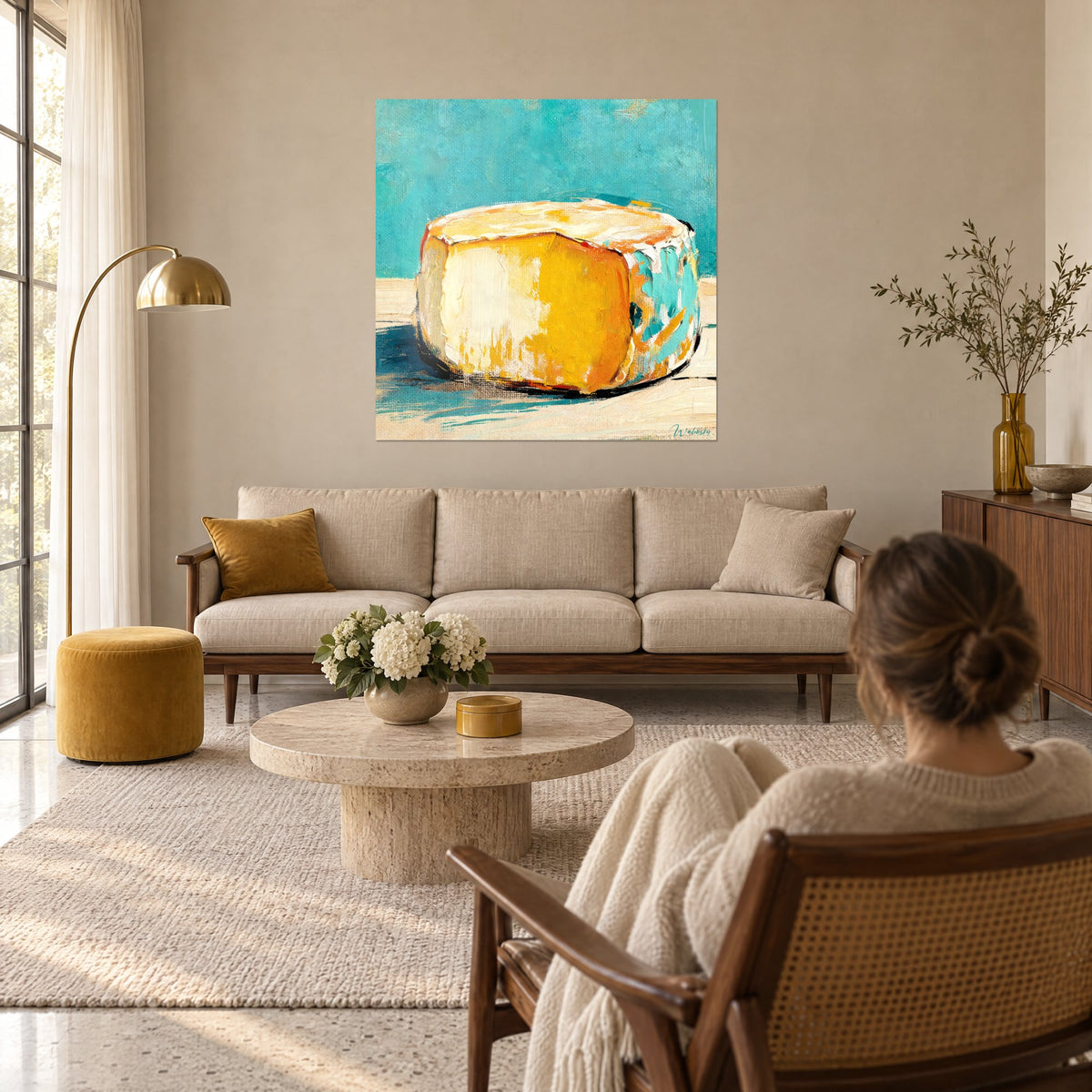Tableau meule de fromage jaune safran, croûte ivoire et fond turquoise, une femme de dos au-dessus d'un canapé dans un salon lumineux
