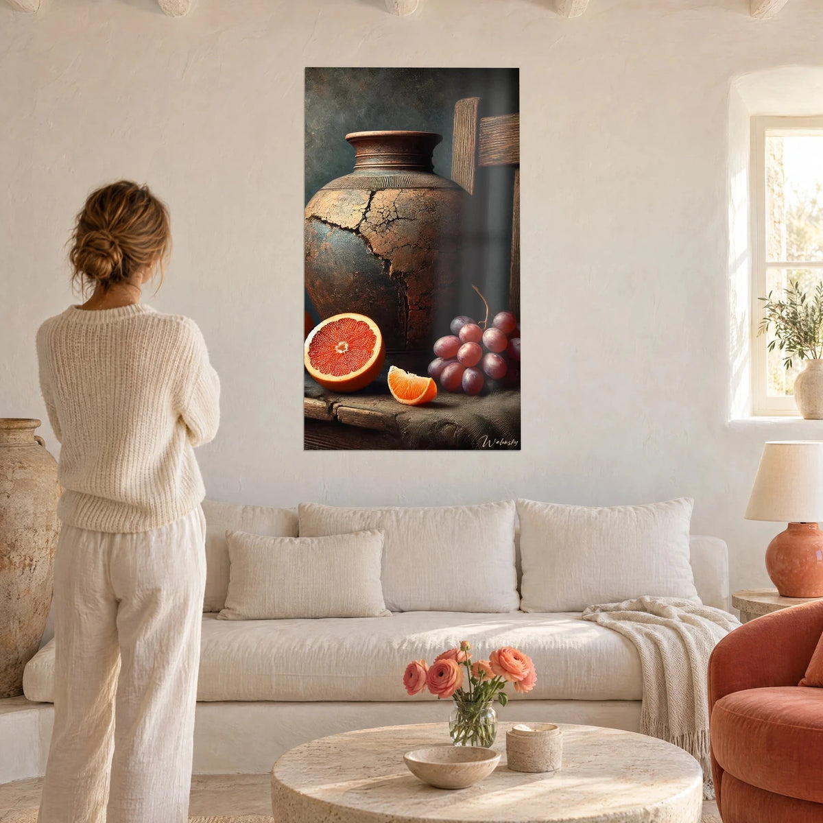 Tableau jarre craquelée cuivrée, pamplemousse rouge et grappe de raisins prune, au-dessus d'un canapé dans un salon lumineux