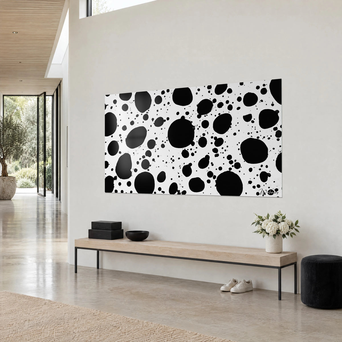 Wall art with a constellation of black drops on pure white background, three-quarter view above a light wooden bench and a pouf