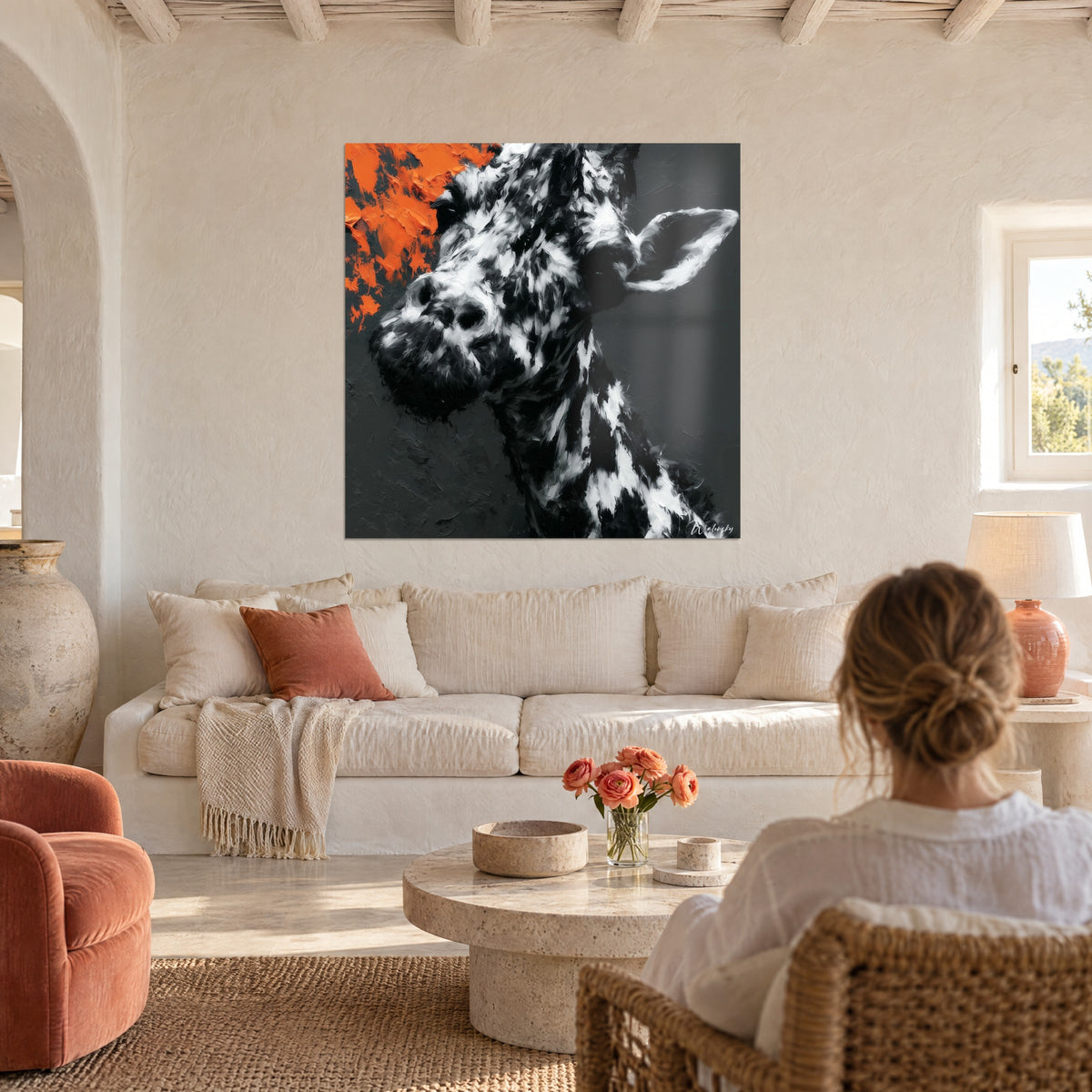 Gemälde Giraffe mit schwarz-weißem Fleckenfell, orangefarbener Farbspritzer oben links, über einem Sofa in einem hellen Wohnzimmer