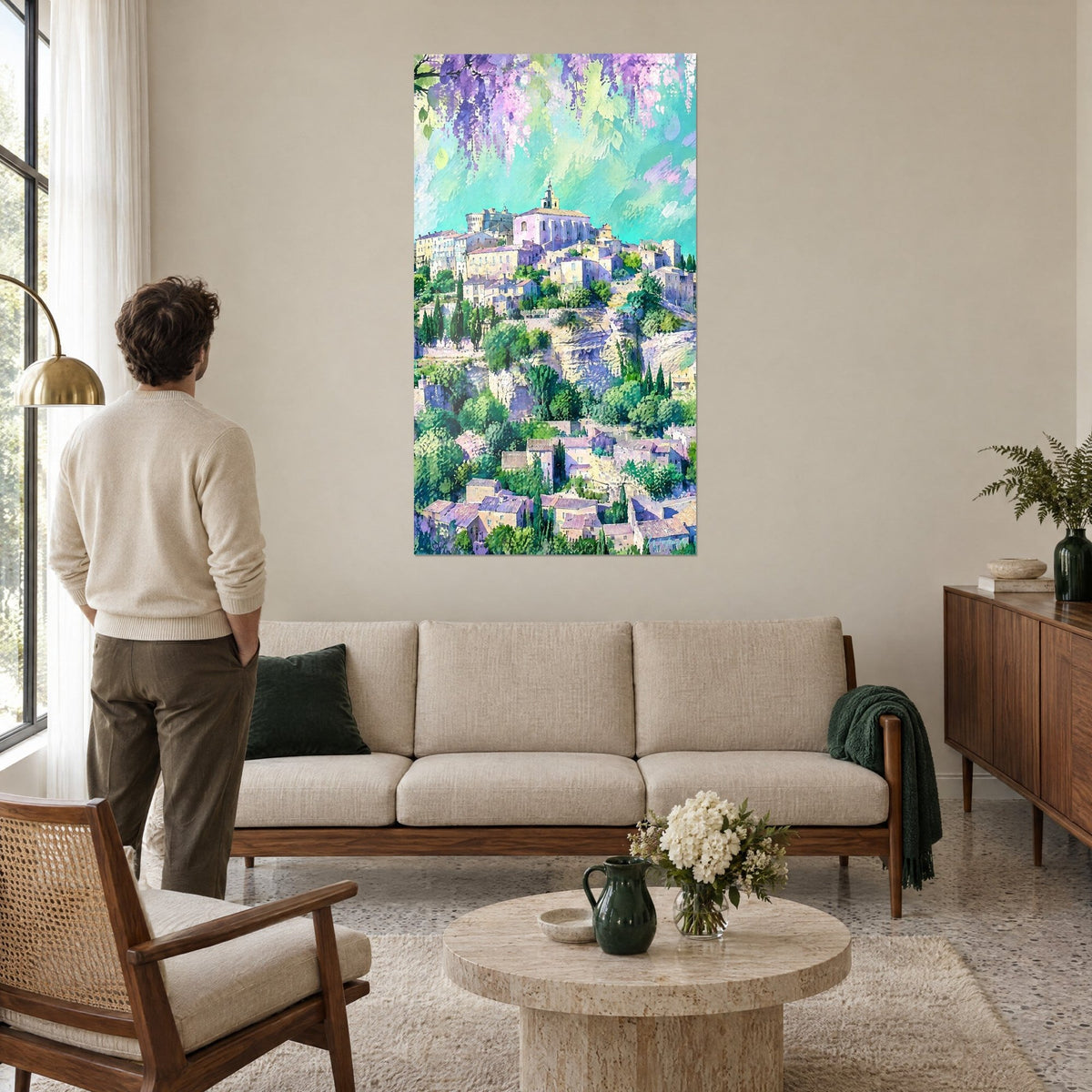Schilderij dorpje op de heuvel met beige huizen onder paarse blauwregen, turquoise lucht, man van achteren, boven een bank in een lichte woonkamer