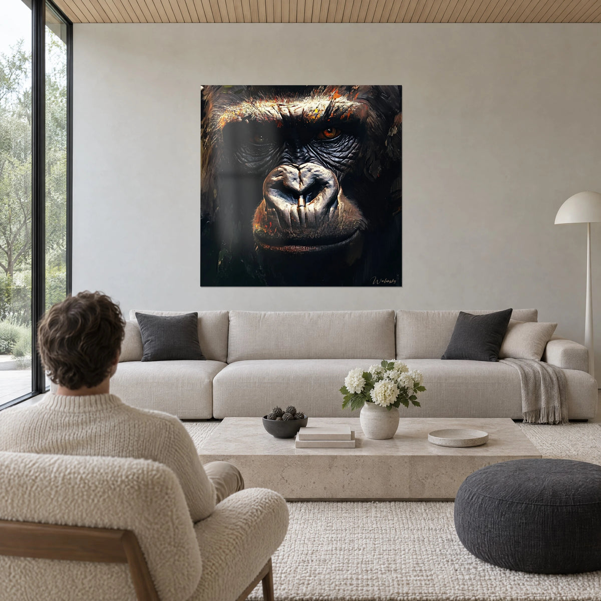 Quadro di gorilla dallo sguardo ambrato, muso grigio perla su fondo nero, uomo di spalle, sopra un divano in un soggiorno luminoso