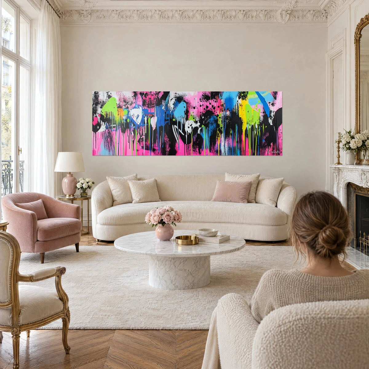 Tableau graffiti aux coulures roses, noires et vert citron, deux personnes de dos le regardent au-dessus d'un canapé dans un salon lumineux