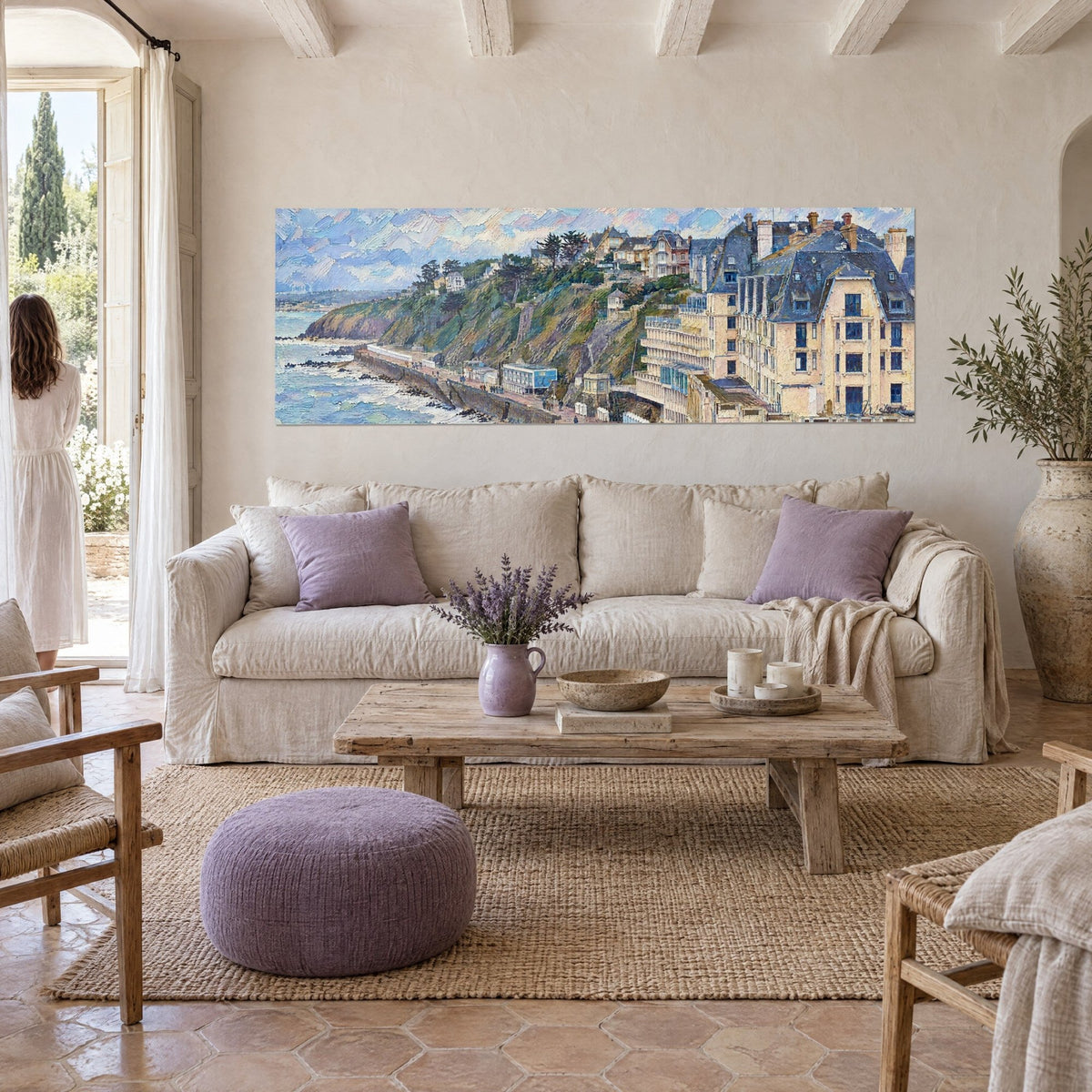 Wall art of a green Normandy cliff overlooking a seaside promenade, beige and blue, above a sofa in a bright living room