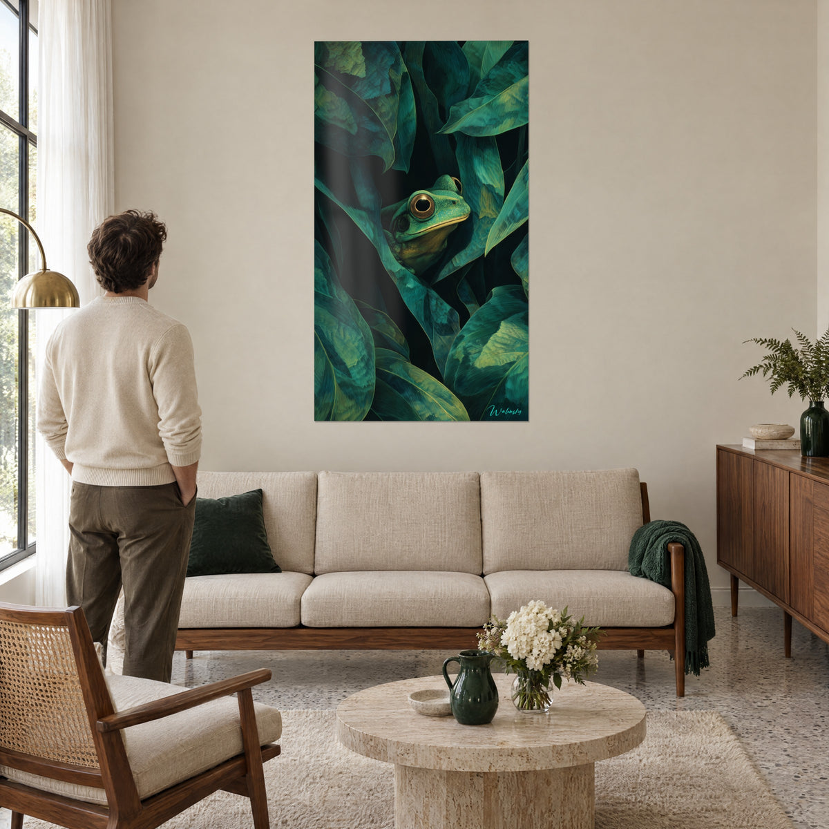 Quadro rana dagli occhi dorati rannicchiata in un fitto fogliame verde profondo, un uomo di spalle la ammira, sopra un divano in un soggiorno luminoso