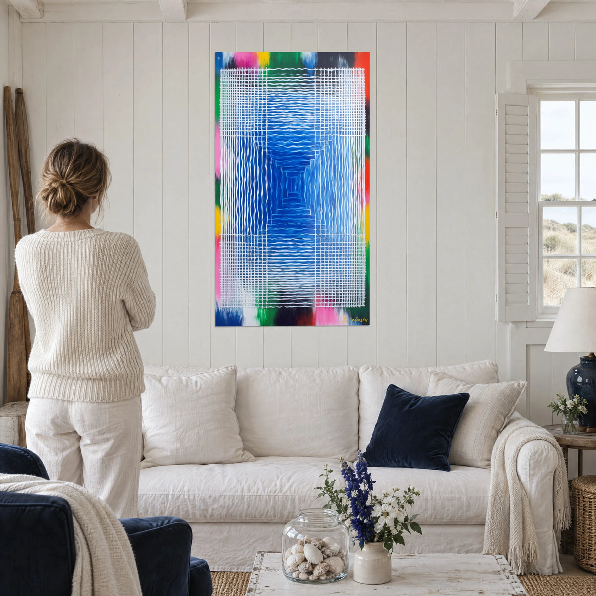 Wall art with a raised white grid over a cobalt blue well, pink and green edges, woman seen from behind, above a sofa in a bright living room