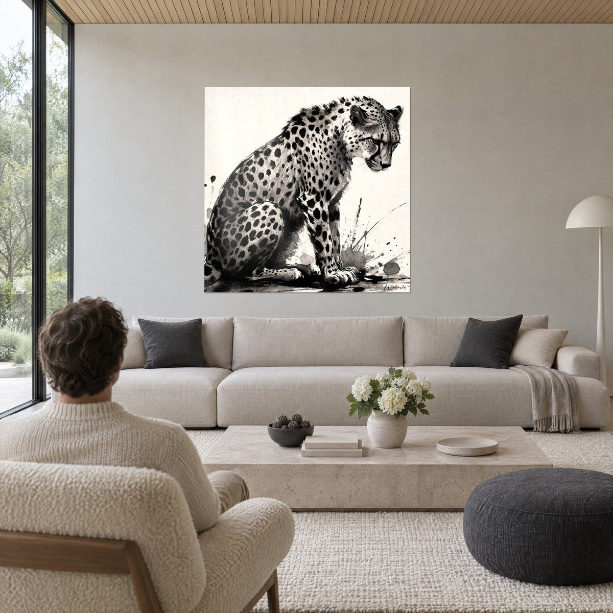 Tableau guépard tacheté assis en encre noire et blanc crème, regard baissé, au-dessus d'un canapé dans un salon lumineux