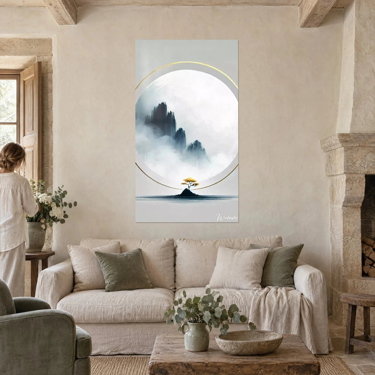 Tableau montagnes brumeuses d'encre bleu-gris dans un cercle blanc, anneau doré, une femme de dos, au-dessus d'un canapé dans un salon lumineux
