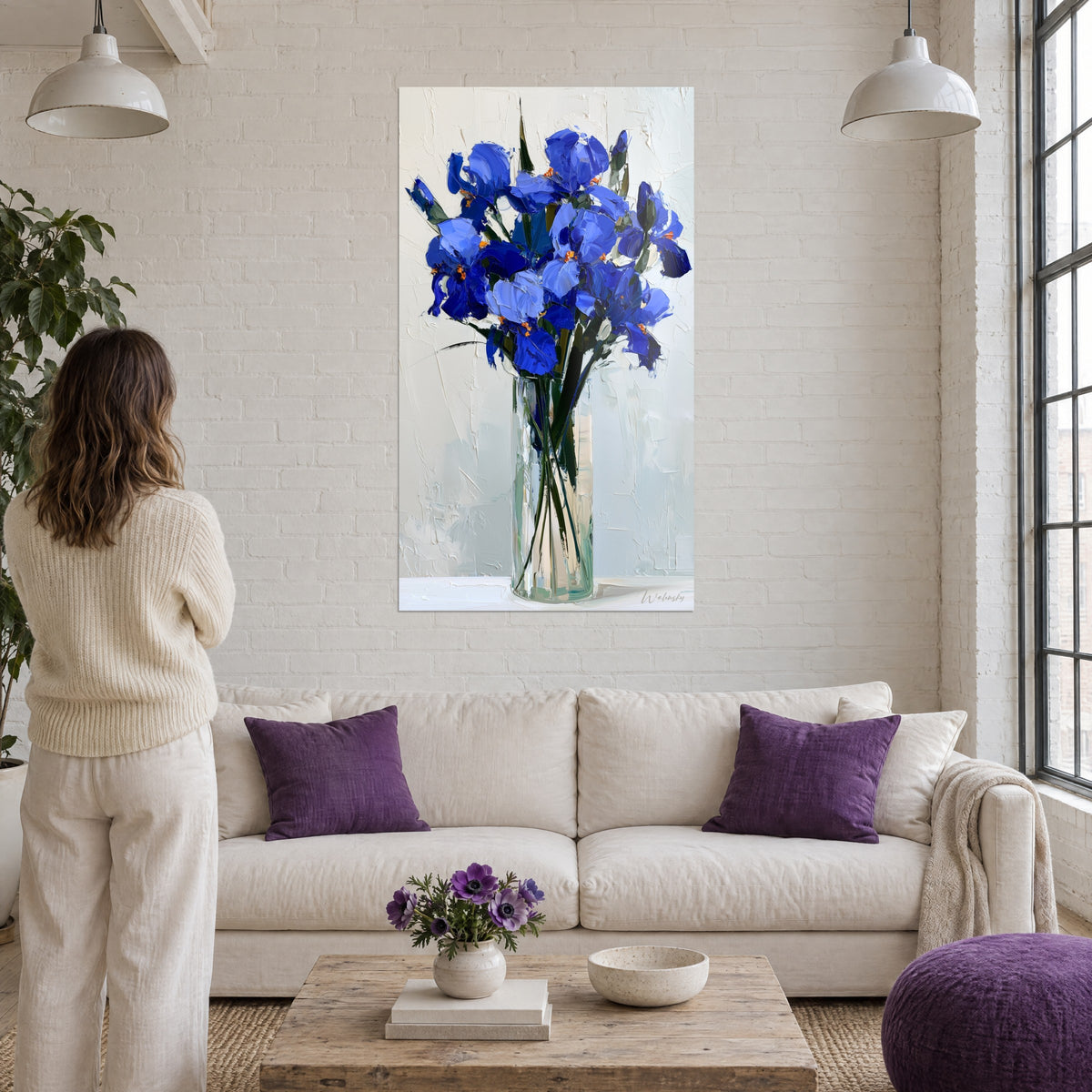 Wall art cobalt blue iris bouquet painted with a palette knife, orange stamens, glass vase, woman seen from behind above a sofa in a bright living room