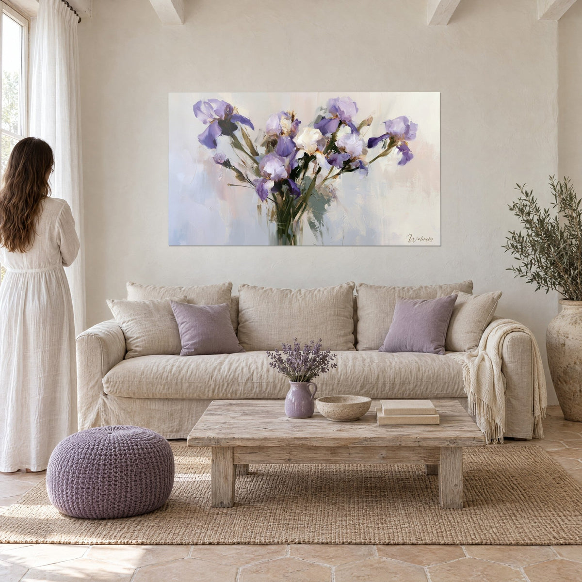 Schilderij boeket paarse en witte irissen in een glazen vaas, saliegroene olieverfstreken, vrouw met de rug naar de kijker, boven een bank in een lichte woonkamer