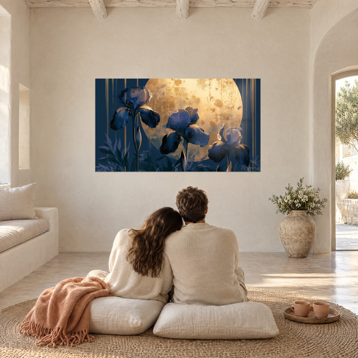 Wall art of three indigo irises standing out against an aged gold moon and fine golden threads, couple seen from behind seated on white cushions