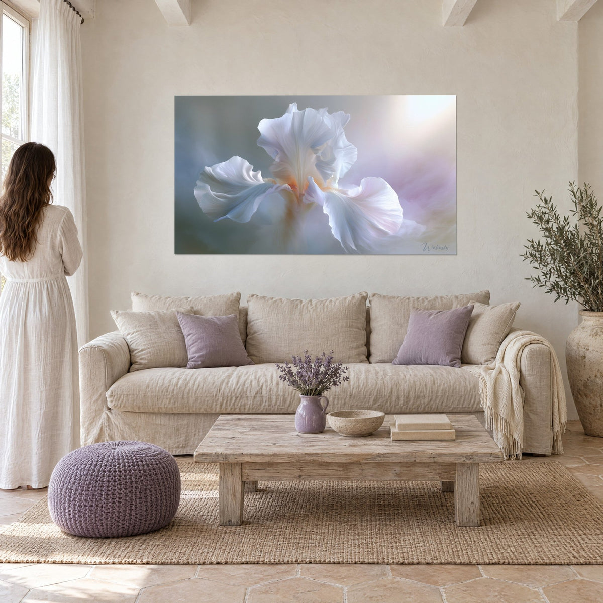 Schilderij van een witte iris met golvende bloemblaadjes, blauwgrijze en zacht roze reflecties, een vrouw van achteren boven een bank in een lichte woonkamer