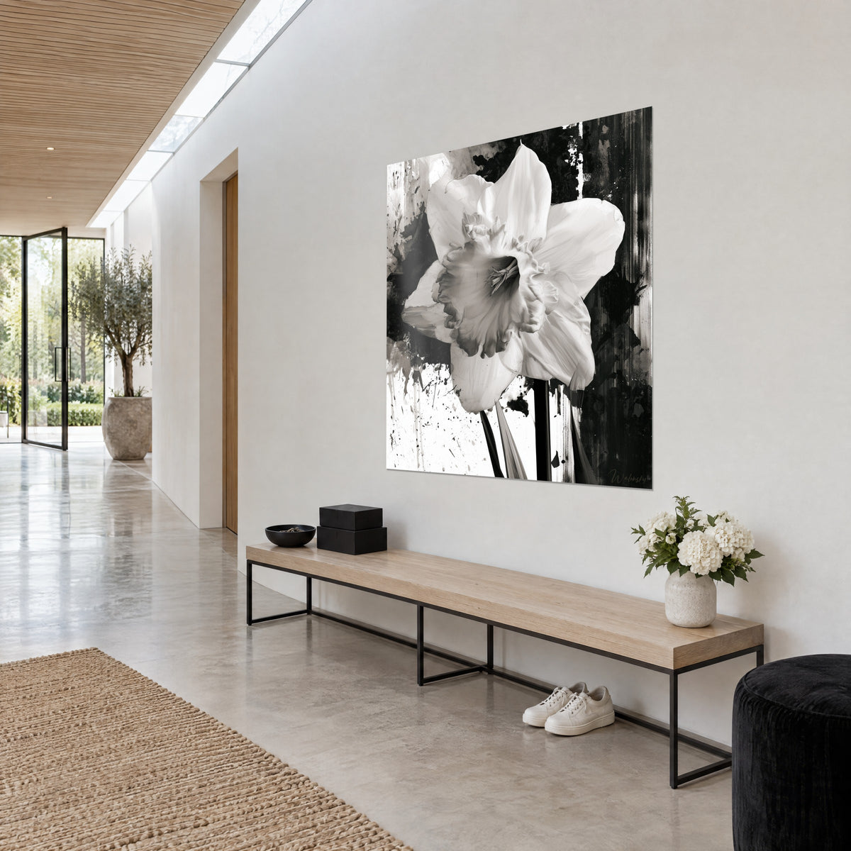 Cuadro trompeta de narciso marfil sobre fondo blanco y negro salpicado de tinta, colgado en un pasillo luminoso sobre el banco de madera