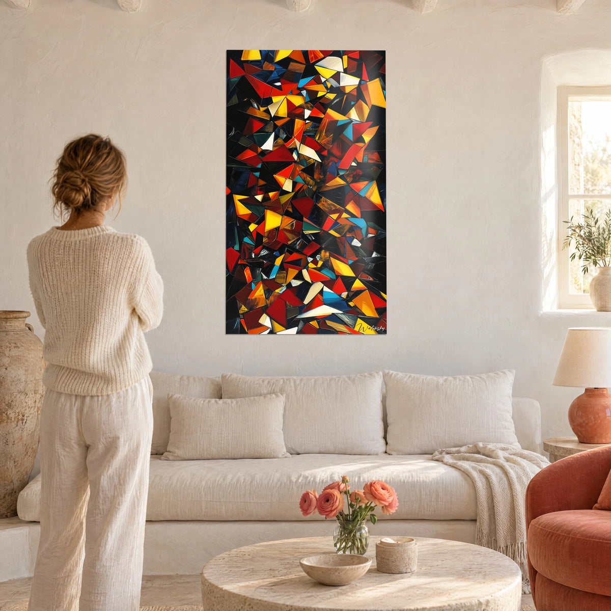 Tableau éclats de verre rouges et jaunes sur fond noir, femme de dos devant, au-dessus d'un canapé dans un salon lumineux