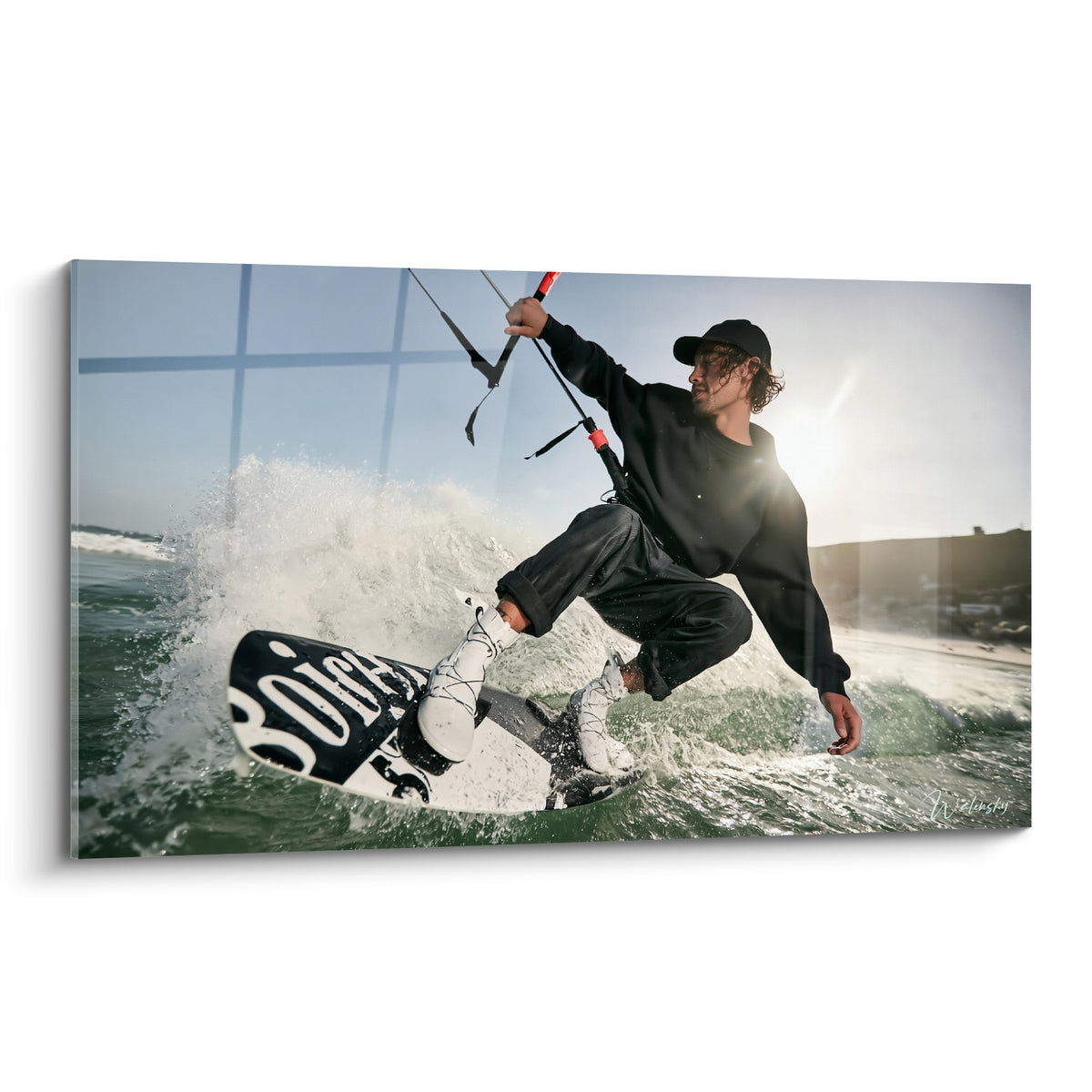Kitesurfeur en saut sur planche noire et blanche, vagues vert émeraude et ciel bleu pastel