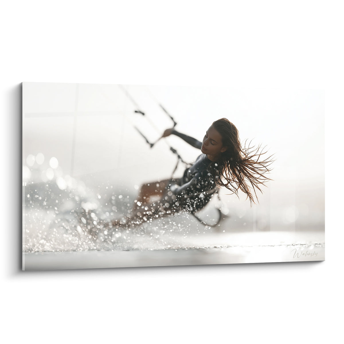 Kitesurfeuse cheveux au vent dans des embruns blancs et gris, glisse sur l'eau lumineuse