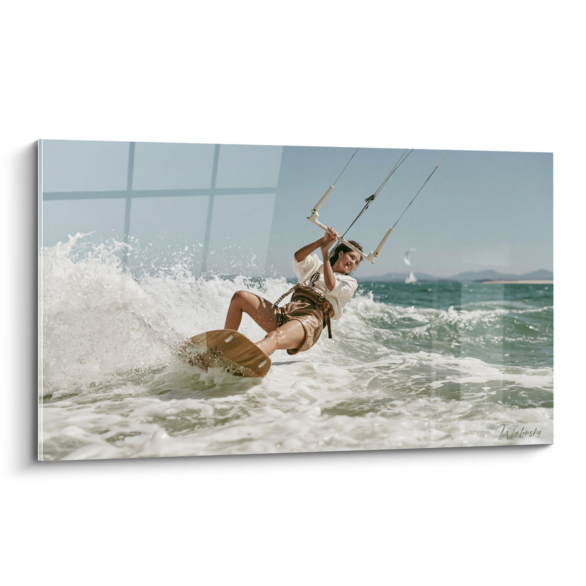 Kitesurfeuse en action fend une vague turquoise et blanche, planche sable et ciel bleu pâle