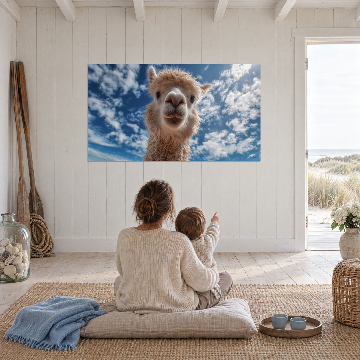 Cuadro de cara de alpaca sonriente, lana beige y blanca, cielo azur nuboso, pared blanca de casa de playa, madre e hijo sentados en el suelo