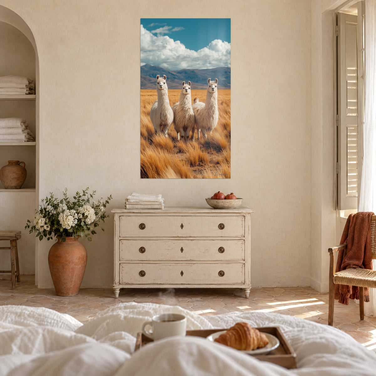 Cuadro alpacas con las orejas erguidas frente a un cielo turquesa, hierbas color azafrán y cumbres marrones, encima de una cama en un dormitorio luminoso