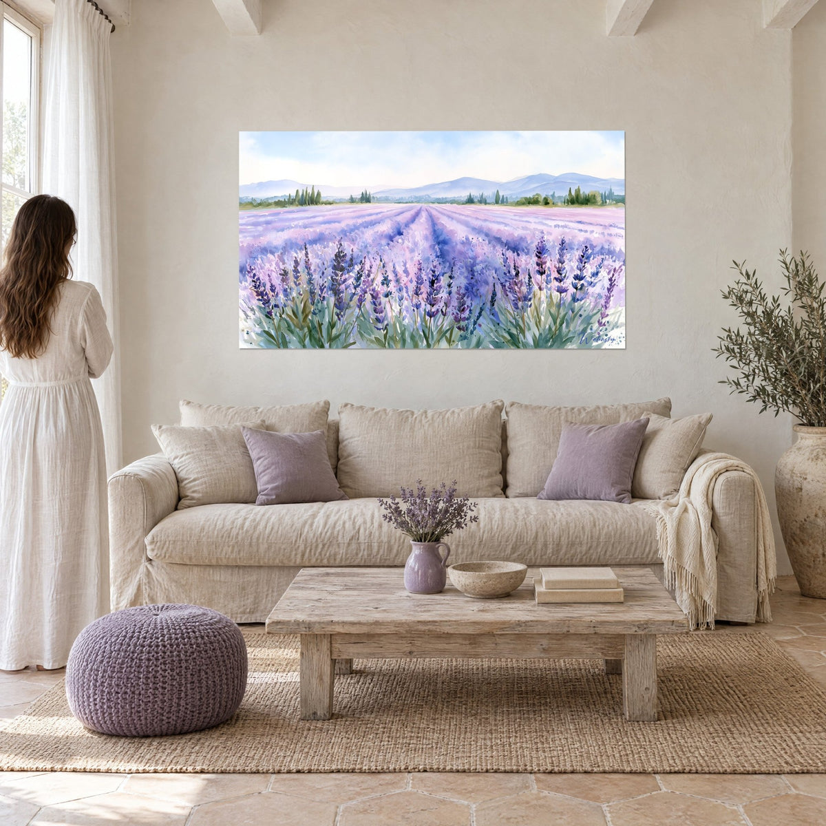 Cuadro campo de lavanda en acuarela, hileras lilas y azules hacia colinas, mujer de espaldas sobre un sofá en un salón luminoso