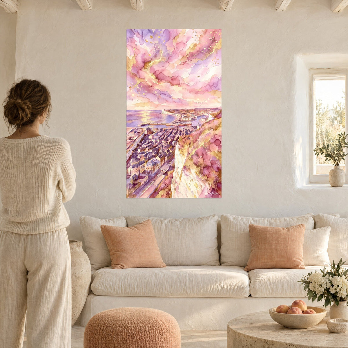 Schilderij witte krijtrots boven de leien daken van Le Tréport, roze en gouden lucht, vrouw van achteren boven een bank in een lichte woonkamer