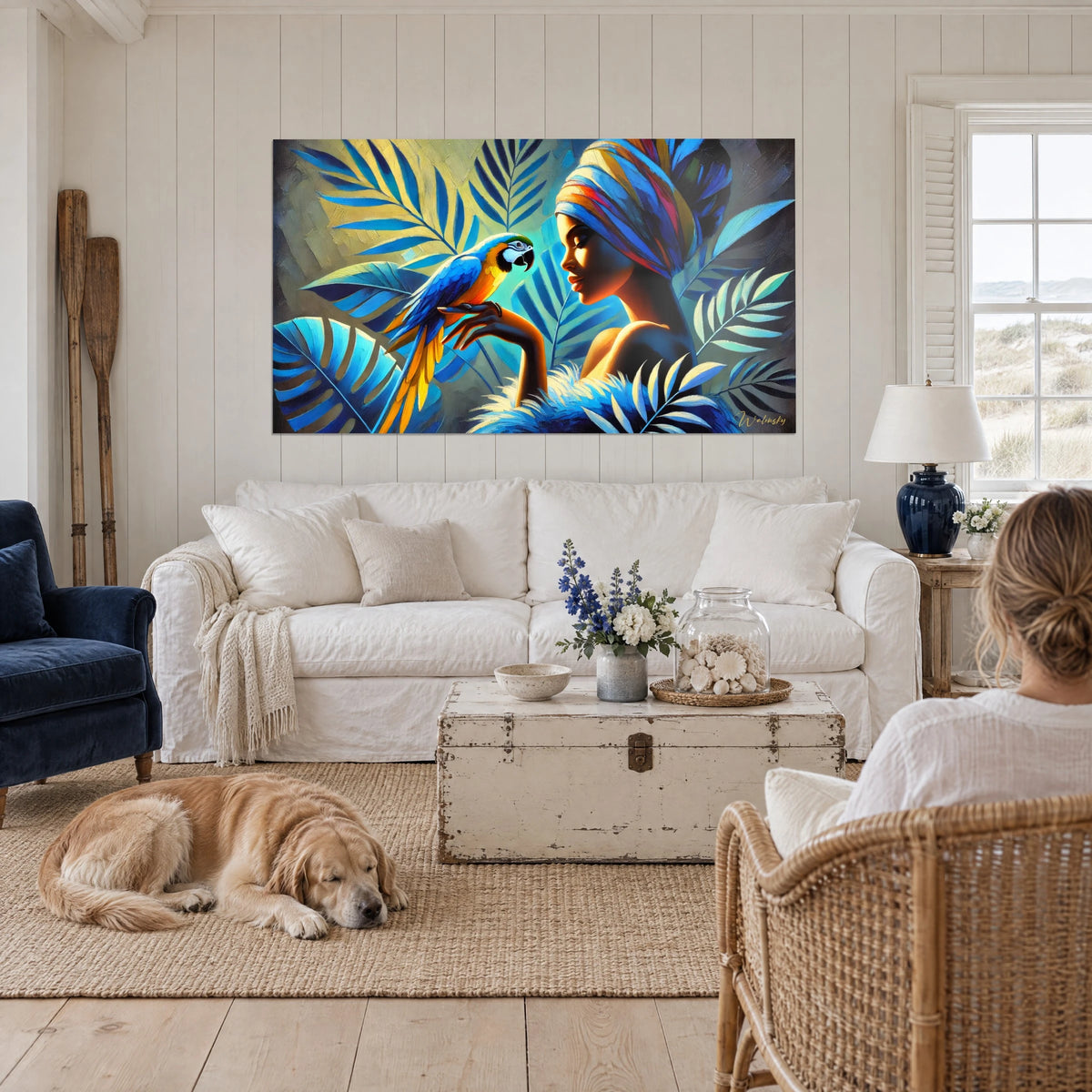Tableau ara bleu et jaune perché sur la main d'une femme au turban, palmes turquoise, au-dessus d'un canapé dans un salon lumineux