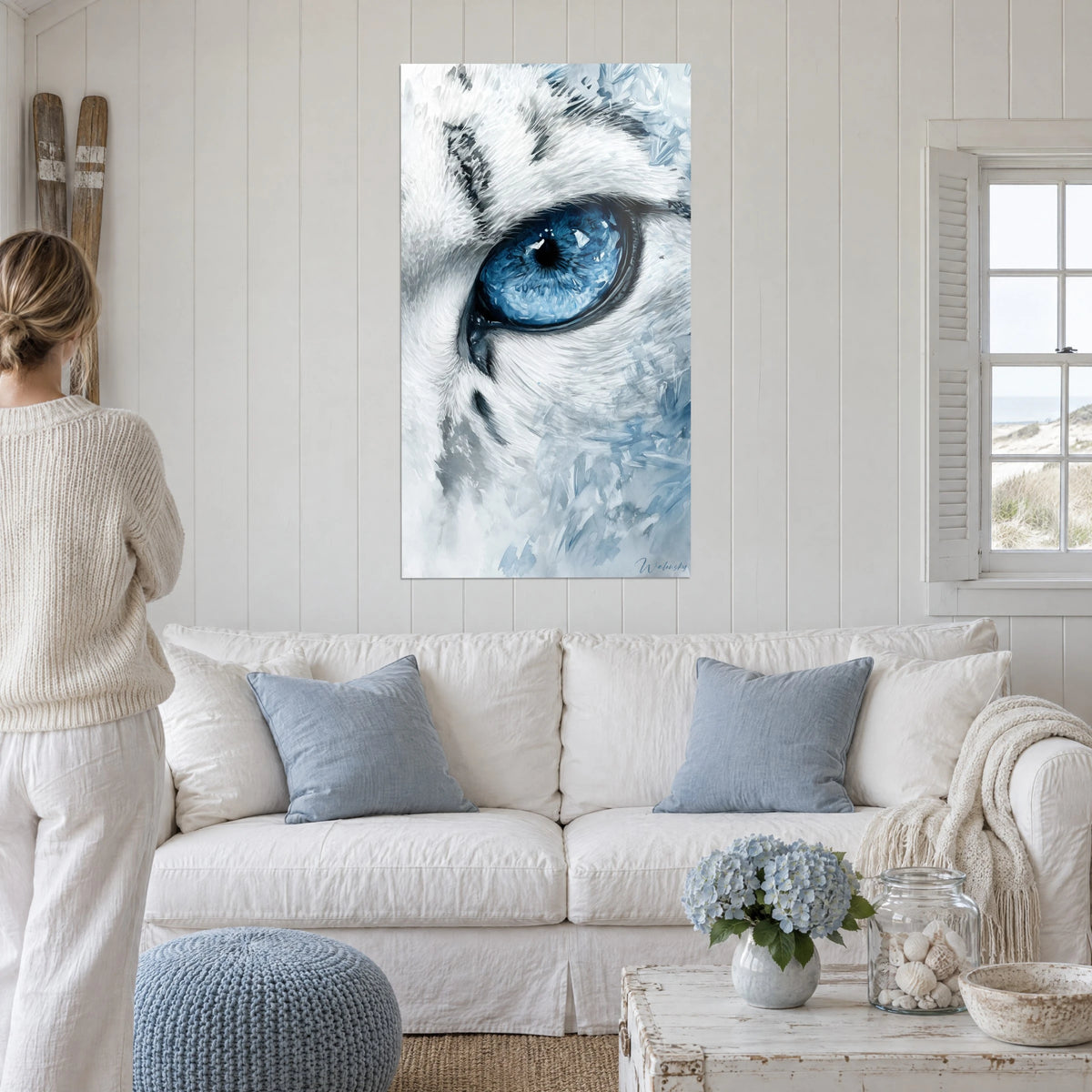 Wall art of a snow cat with glacier-blue iris, white and grey fur, above a sofa in a bright living room