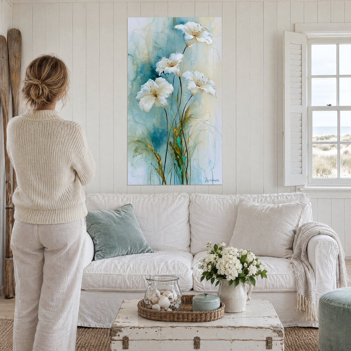 Tableau lys blancs sur fond bleu turquoise et tiges noires graciles, femme de dos, au-dessus d'un canapé dans un salon lumineux