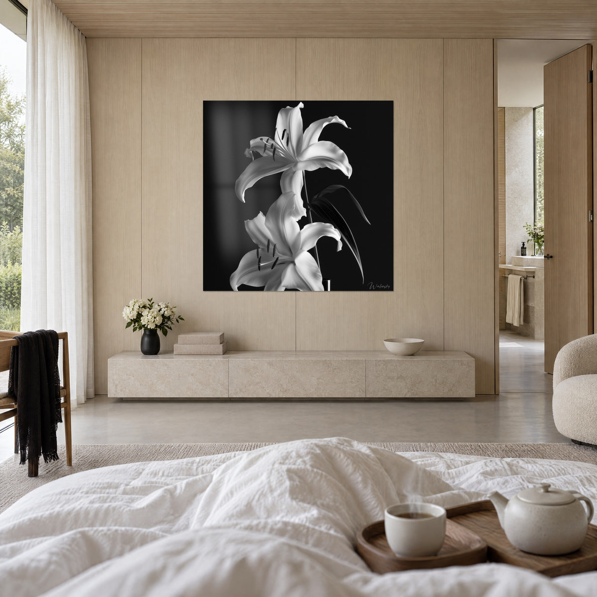 Cuadro de una corola impecable sobre un fondo negro profundo, estambres color carbón y tallo gris, una persona de espaldas, encima de una cama en un dormitorio luminoso