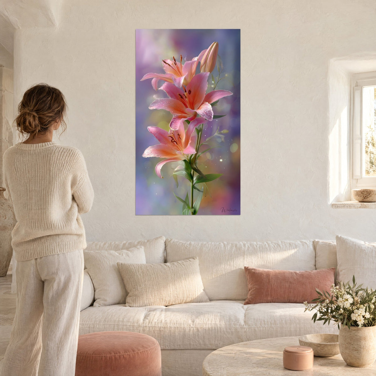 Quadro giglio rosa tenue perlato di rugiada, petali color salmone su sfondo malva, visto da una donna di spalle, sopra un divano in un soggiorno luminoso