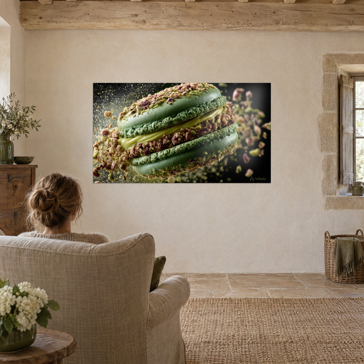 Wall art almond green soft shells and golden ganache dotted with brown pistachios, admired by a woman in a linen armchair