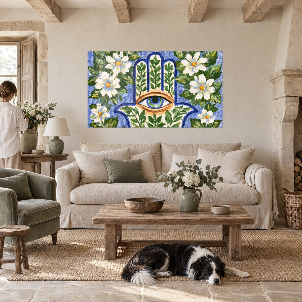 Tableau main de fatma ornée d'un œil vert, entourée de marguerites blanches sur fond bleu, au-dessus d'un canapé dans un salon lumineux