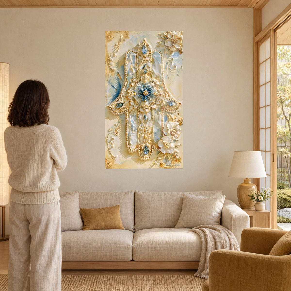 Tableau main de fatma ivoire ornée de perles nacrées et de gemmes bleues, fleur bleutée au centre, au-dessus d'un canapé dans un salon lumineux