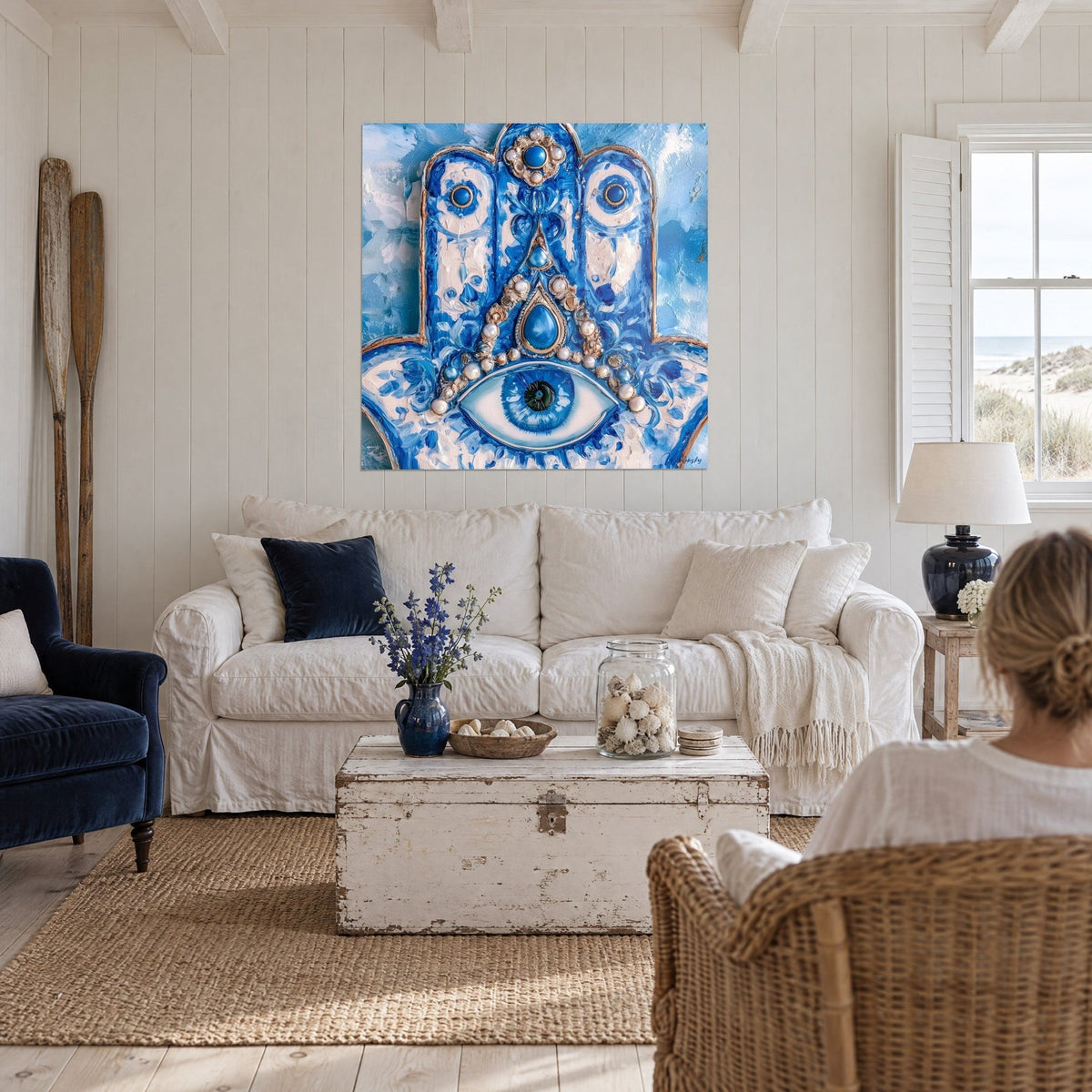 Tableau hamsa peint en bleu cobalt et blanc crème, œil central à perles, au-dessus d'un canapé dans un salon lumineux