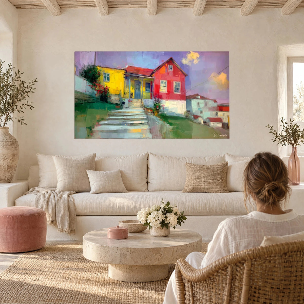 Tableau maisonnette jaune et bâtisse rouge dominant un escalier pâle, ciel mauve, couple de dos au-dessus d'un canapé dans un salon lumineux