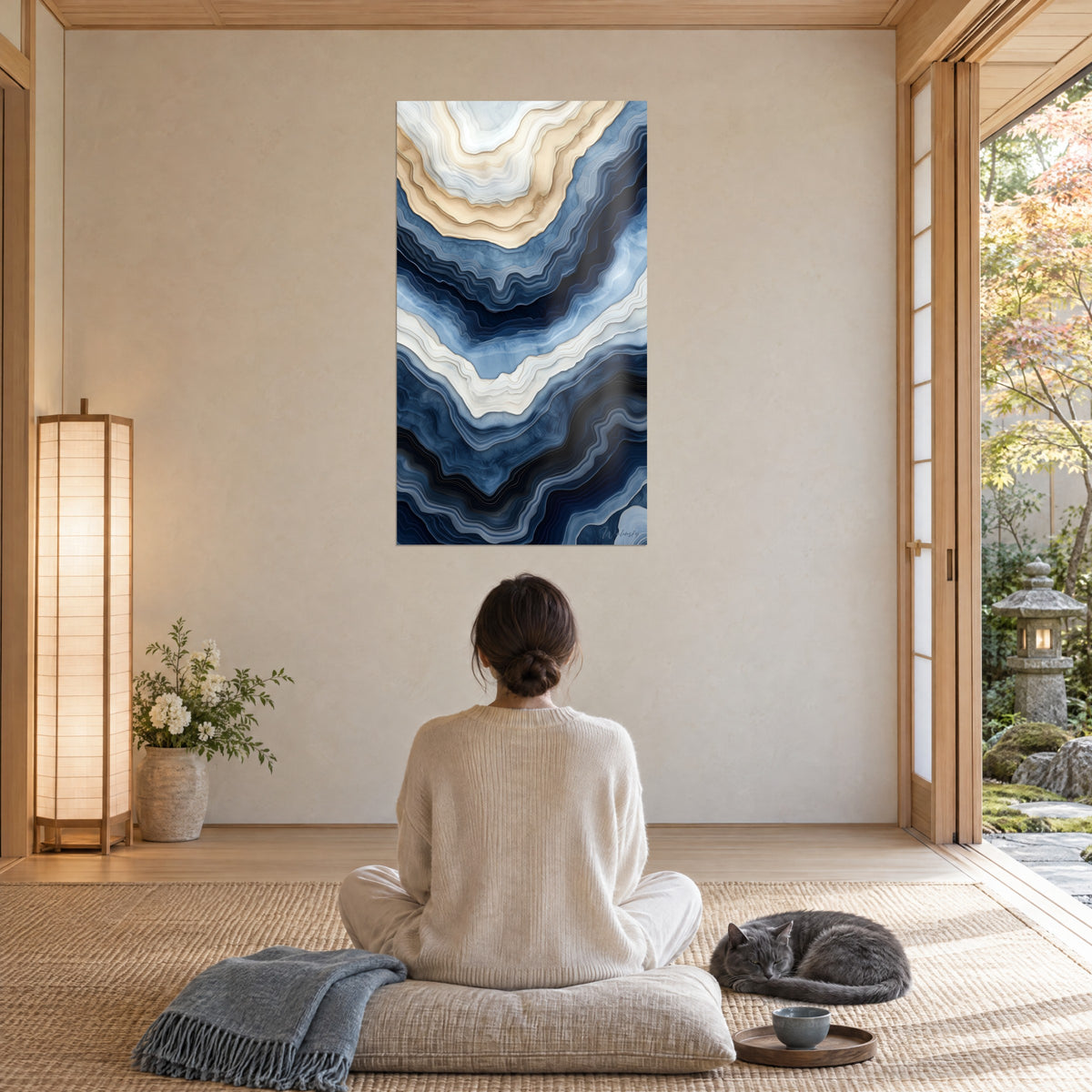 Cuadro degradados azul acero y crema en estratos de piedra, gato gris ovillado sobre un cojín delante, salón japandi